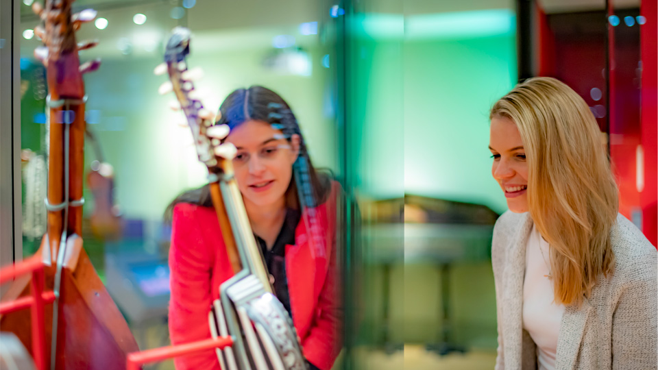 Two adult white female students looking at an exhibit, in a brightly lit room at the Royal College of Music museum.
